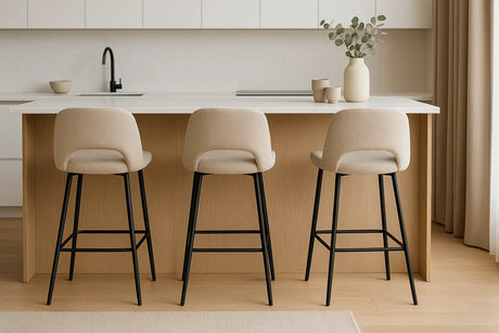 Drie beige barkrukken met zwarte poten aan een licht houten keukeneiland in een moderne minimalistische keuken.