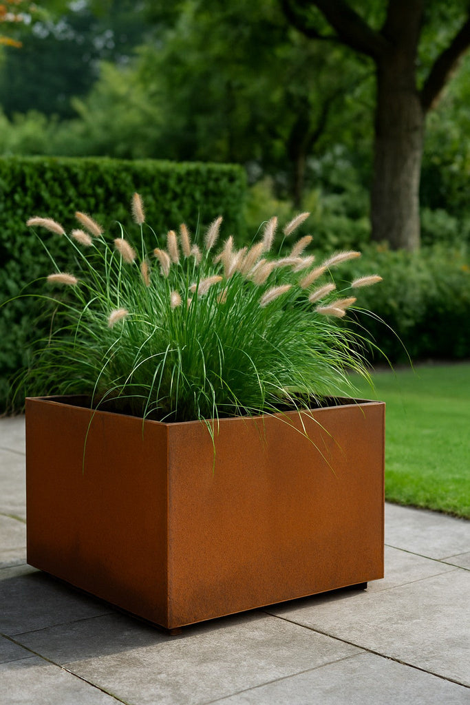 Cortenstalen plantenbak met siergras op een betegeld terras in een groene tuin