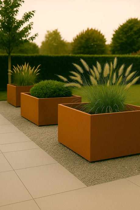 Moderne tuin met drie cortenstaal plantenbakken gevuld met siergrassen en buxus, geplaatst op een grindstrook naast grote terrastegels.